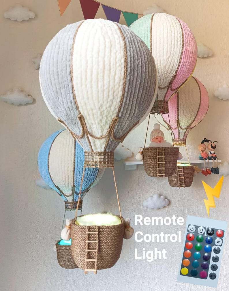 May include: Three white, grey, and pink hot air balloon-shaped lamps with a rope basket and a remote control for changing the light colour. The text "Remote Control Light" is written below the balloons.
