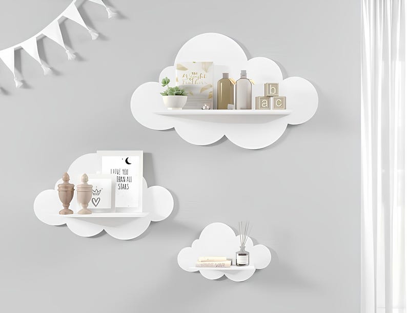 May include: Three white cloud-shaped shelves mounted on a white wall. The top shelf has two bottles and three wooden blocks with letters. The middle shelf has two decorative items and a framed print with the text "I love you to the moon and all stars". The bottom shelf has a small decorative item and a diffuser.
