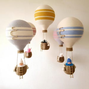 May include: Five handmade hot air balloons with different colored stripes and patterns. Each balloon has a basket with a small stuffed animal or plant inside. The balloons are hanging from the ceiling.