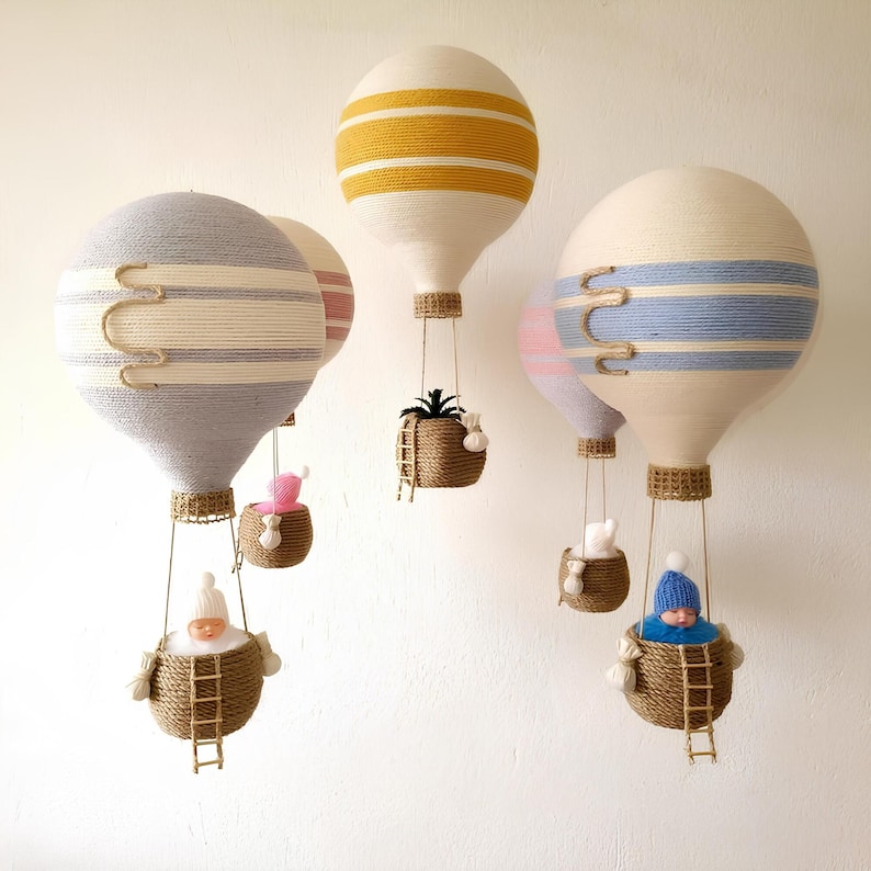 May include: Five handmade hot air balloons with different colored stripes and patterns. Each balloon has a basket with a small stuffed animal or plant inside. The balloons are hanging from the ceiling.