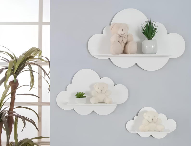 May include: Three white cloud-shaped shelves with rounded edges, mounted on a light gray wall. The top shelf has a small potted plant and a plush teddy bear. The middle shelf has a small potted plant and a plush teddy bear. The bottom shelf has a plush teddy bear.