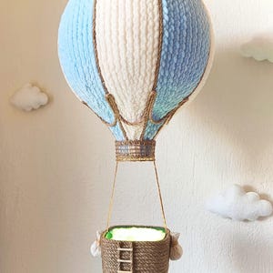 May include: A blue and white yarn hot air balloon with a brown rope basket and a small wooden ladder. The balloon is hanging from the ceiling.