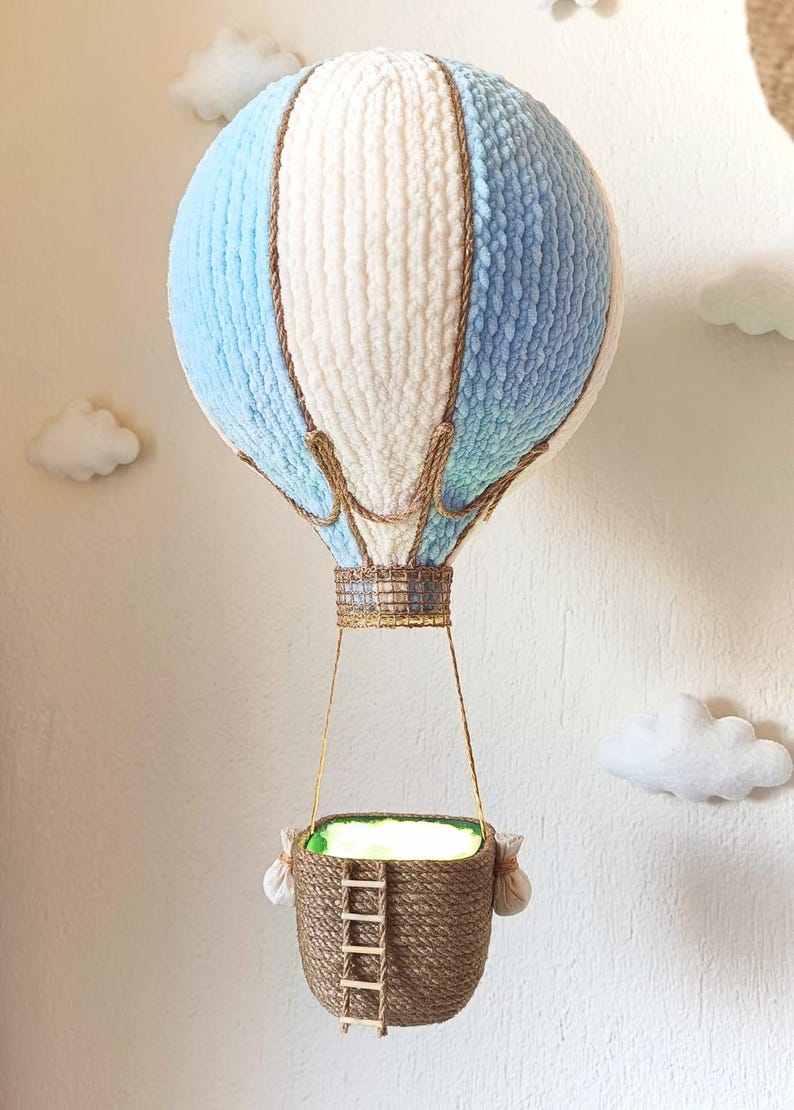 May include: A blue and white yarn hot air balloon with a brown rope basket and a small wooden ladder. The balloon is hanging from the ceiling.
