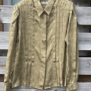 Pode incluir: Camisa dourada de manga comprida com estampa paisley. A camisa tem pregas na frente e uma gola clássica. A etiqueta diz "Le Claire".
