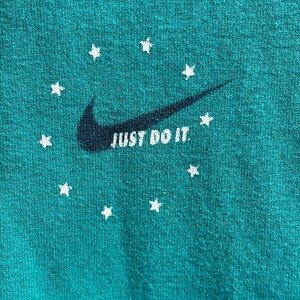 May include: Teal fabric featuring a dark navy Nike swoosh and the words "JUST DO IT" in white. White star shapes encircle the swoosh. The fabric has a textured appearance.