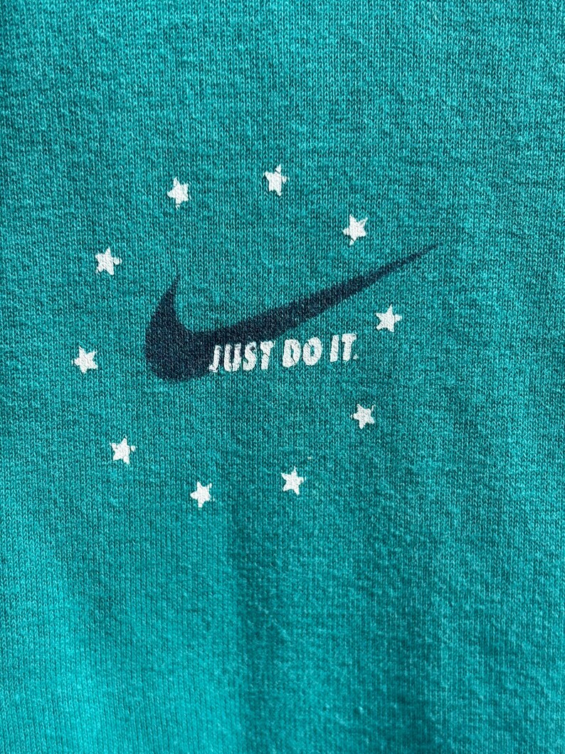 May include: Teal fabric featuring a dark navy Nike swoosh and the words "JUST DO IT" in white. White star shapes encircle the swoosh. The fabric has a textured appearance.