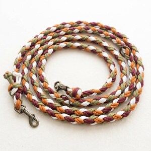 May include: Braided dog lead in a spiral design. The lead is multi-coloured, with white, olive green, orange, and burgundy strands. It has a metal clasp and a loop for easy handling.
