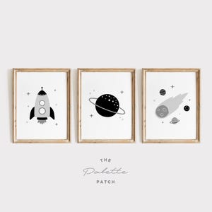May include: Three black and white illustrations in wooden frames. The illustrations are of a rocket, a planet with rings, and a comet. The frames are hung on a white wall.