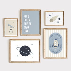 May include: A set of five framed art prints with a space theme. The prints feature a telescope, a countdown, a comet, a planet with a ring, and a rocket ship with the text "We're going to the moon". The color palette includes blue, beige, and white.
