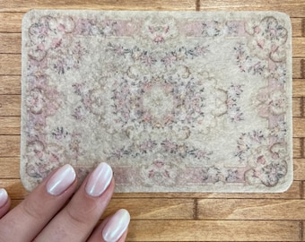 May include: A small, beige rug with a pink and gray floral pattern. The rug is made of a soft, fuzzy material.