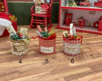 May include: Miniature Christmas-themed gift boxes. One is gold with "Christmas Memories" text, another is red with "Merry Christmas" text, and the third is red with "Compliments of the Season" text. Each box contains decorative elements.