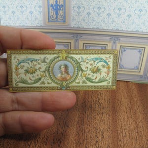 May include: A decorative wall panel with a gold frame and a floral design. The centre of the panel features a portrait of a woman with a crown of flowers.