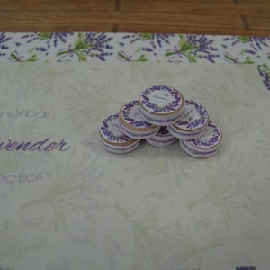 May include: A stack of six round, white and gold-rimmed tins with the words "herbal lavender collection" printed on a white background.