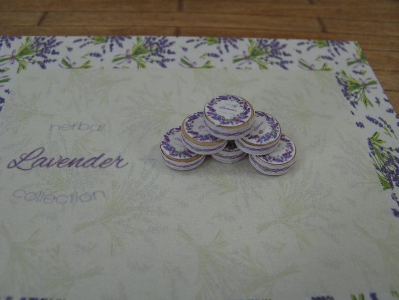 May include: A stack of six round, white and gold-rimmed tins with the words "herbal lavender collection" printed on a white background.