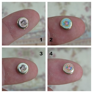 Peut inclure: Quatre petits boutons ronds en céramique avec une bordure dorée. Deux boutons présentent un motif floral en rose, bleu et vert. Les deux autres boutons présentent un portrait d'une femme dans une robe rose et blanche.