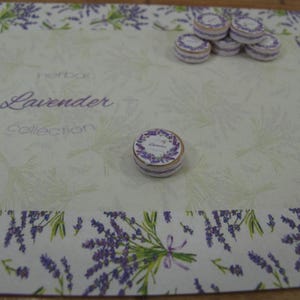 May include: A white background with a lavender design border. The text "Herb Box Lavender Collection" is printed in the centre. There are several small round boxes with a lavender design on top of the boxes.