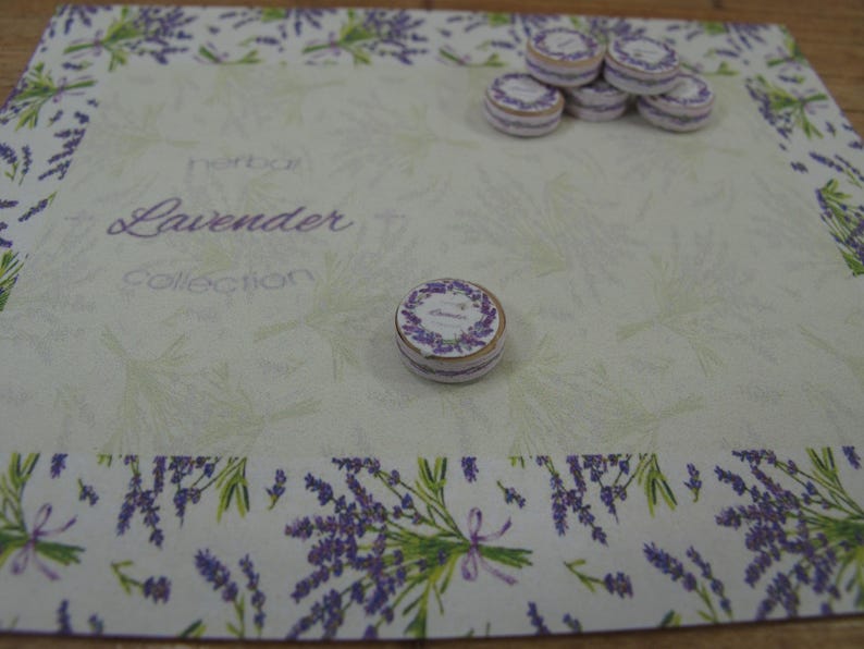 May include: A white background with a lavender design border. The text "Herb Box Lavender Collection" is printed in the centre. There are several small round boxes with a lavender design on top of the boxes.