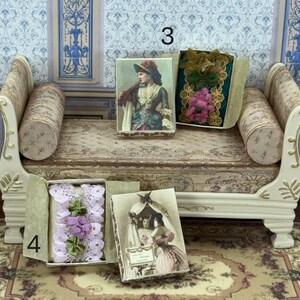 Può includere: Accessori per case delle bambole in miniatura tra cui quattro piccole scatole. Una scatola contiene un ritratto d'epoca, un'altra ha una composizione floreale e una terza ha finiture in pizzo con accenti verdi e viola. La quarta scatola presenta un ritratto di due donne.