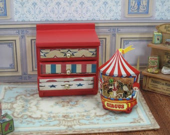 May include: Miniature red wooden dresser with three drawers, each decorated with patriotic patterns and gold knobs. A circus-themed carousel with a red and white striped tent and the word "CIRCUS" is also featured.