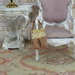 May include: A brown fabric handbag with a lace trim and a gold button closure. The bag is hanging on the back of a white chair with a pink cushion.