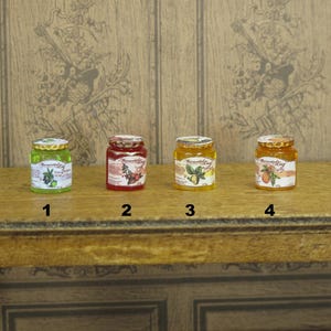 Könnte beinhalten: Vier Miniaturgläser mit Marmelade, die verschiedene Fruchtmotive und Etiketten zeigen. Die Gläser sind in einer Reihe auf einer Holzoberfläche angeordnet. Die Etiketten tragen die Aufschrift "Remarkable" und zeigen Bilder von Beeren, Birnen und Zitrusfrüchten.