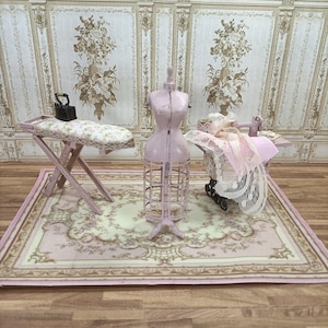 Könnte beinhalten: Eine Miniatur-Puppenhausszene mit einem rosa-weißen Bügelbrett, einer rosa-weißen Schaufensterpuppe, einer rosa-weißen Nähmaschine und einem rosa-weißen Teppich mit Blumenmuster.