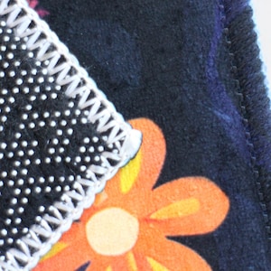 Pu&ograve; includere: Primo piano di un tessuto con motivo bianco e nero con un bordo cucito bianco. Il tessuto presenta un motivo floreale con fiori arancioni, gialli e bianchi.