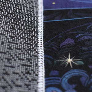 Pu&ograve; includere: Primo piano del bordo di un tappeto blu scuro con un bordo bianco. Il tappeto presenta un motivo dettagliato di stelle e volute.