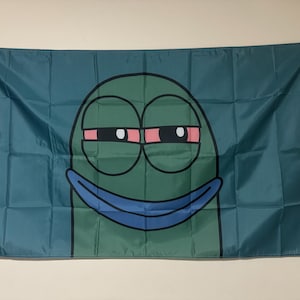 Peut inclure: Un personnage de dessin anim&eacute; vert avec un large sourire et des yeux cercl&eacute;s de rouge. Le personnage est sur un fond bleu.