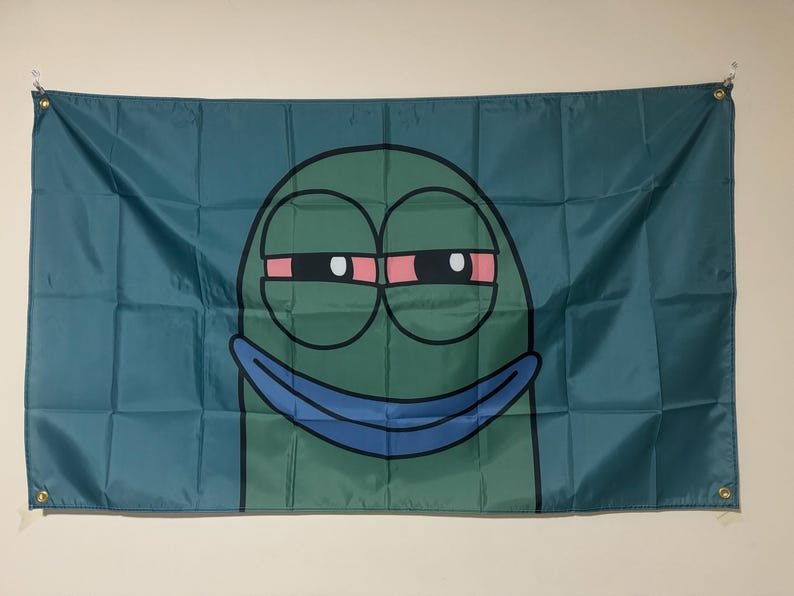 Peut inclure: Un personnage de dessin anim&eacute; vert avec un large sourire et des yeux cercl&eacute;s de rouge. Le personnage est sur un fond bleu.