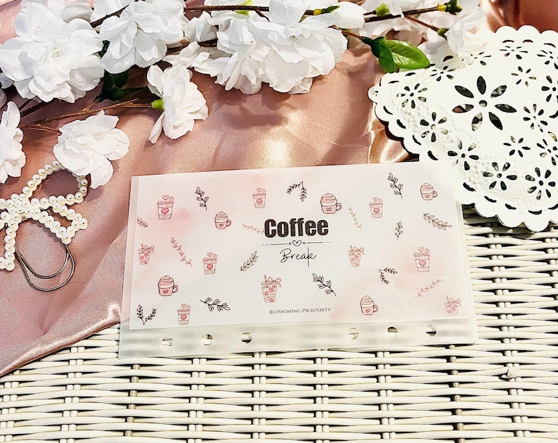 Peut inclure: Un organiseur transparent pour pause-caf&eacute; avec un fond rose aquarelle et des illustrations de tasses &agrave; caf&eacute;. Les mots "Coffee Break" sont imprim&eacute;s en noir. L'organisateur comporte plusieurs trous pour la reliure et est orn&eacute; d'&eacute;l&eacute;ments floraux.