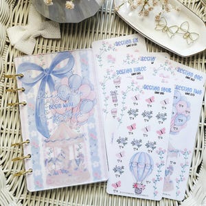Puede incluir: Una agenda de discos con una cubierta de carrusel y globos en azul y rosa que incluye el texto Fairy tales BEGIN WITH tiny steps, acompañada de varias hojas de pegatinas etiquetadas de Section One a Section Six con diseños florales.