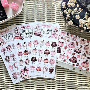 May include: Three vertical sticker sheets and one horizontal sticker sheet featuring pink and brown autumn-themed illustrations of pumpkins, sweaters, bows, and mugs. The text reads Leaf by Leaf, Hello Pumpkin, and Autumn Bliss with small heart icons.