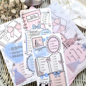 Puede incluir: Una colección de tarjetas decorativas para planificador con diseños en rosa pastel y azul. Las tarjetas presentan ilustraciones de vestidos, lazos y texto como "To My Future Self" y "Confessions of a..." en un estilo manuscrito. Las tarjetas están dispuestas sobre una superficie tejida.