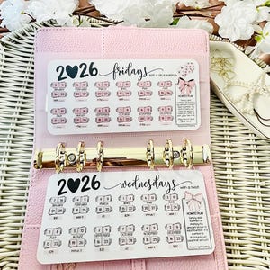 Op de afbeelding: Een roze planner met gouden ringen, open om twee inzetstukken voor 2026 te laten zien. Eén inzetstuk is gelabeld met "Vrijdagen" en de andere met "Woensdagen". Elk inzetstuk heeft een kalenderindeling met data en instructies.