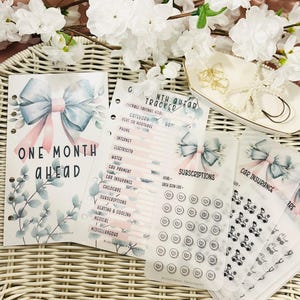 Op de afbeelding: Planner inserts met een aquarel strik ontwerp in blauw en roze. De inserts bevatten een "One Month Ahead" pagina, een maandelijkse tracker en pagina's voor abonnementen en autoverzekeringen. De tekst "Blooming Prosperity" is zichtbaar.