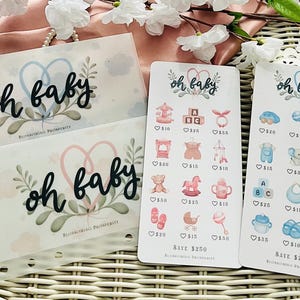 Può includere: Set di cancelleria a tema baby con buste trasparenti e biglietti con la scritta "oh baby". I biglietti presentano illustrazioni e prezzi relativi ai bambini. Il set è decorato con disegni floreali e a forma di cuore.