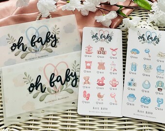 以下が含まれることがあります： 「oh baby」の文字が入った、透明なポーチとカードが特徴のベビーテーマの文房具セット。カードにはベビー関連のイラストと価格が表示されています。セットは花柄とハートのデザインで装飾されています。