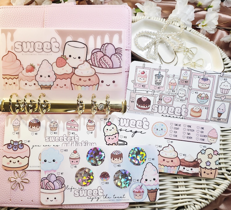 Op de afbeelding: Een roze planner met gouden ringen, gevuld met decoratieve stickers en inlegvellen met schattige illustraties van cupcakes, ijs en macarons. Het woord "sweet" is zichtbaar op verschillende inlegvellen.