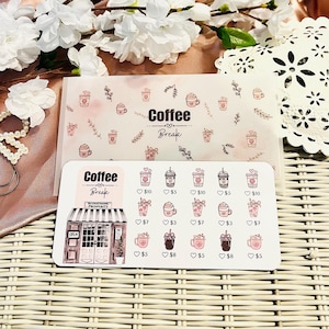 Peut inclure: Une feuille d'autocollants et une carte avec les mots "Coffee Break" et des illustrations sur le th&egrave;me du caf&eacute;. La feuille d'autocollants pr&eacute;sente diverses boissons au caf&eacute; avec des prix. La carte a un design similaire avec des ic&ocirc;nes de tasses &agrave; caf&eacute;.