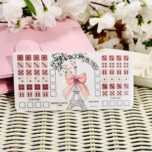 May include: A sticker sheet with a pink and white design. The sheet features dice, the Eiffel Tower, and the text "Roll the Dice & Blooms in Paris". There are boxes for tracking savings.
