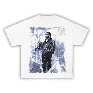 May include: White t-shirt featuring a graphic of a person in a black jacket and pants, set against a blue and white icy background. The design is centered on the shirt.