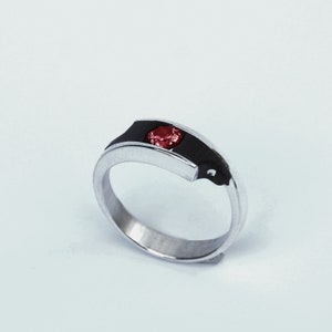 Peut inclure: Une bague en argent avec une incrustation noire et une pierre précieuse rouge. La bague est conçue avec une forme angulaire unique.