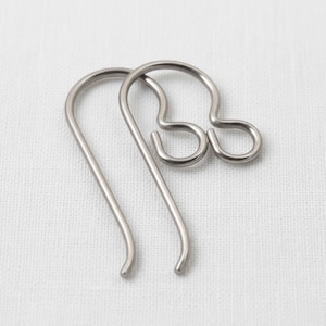 May include: Two silver-toned metal earring hooks with a smooth, curved design. Each hook features a rounded top loop for attachment and a long, slender wire that curves downward, designed for insertion into the earlobe for jewelry making.
