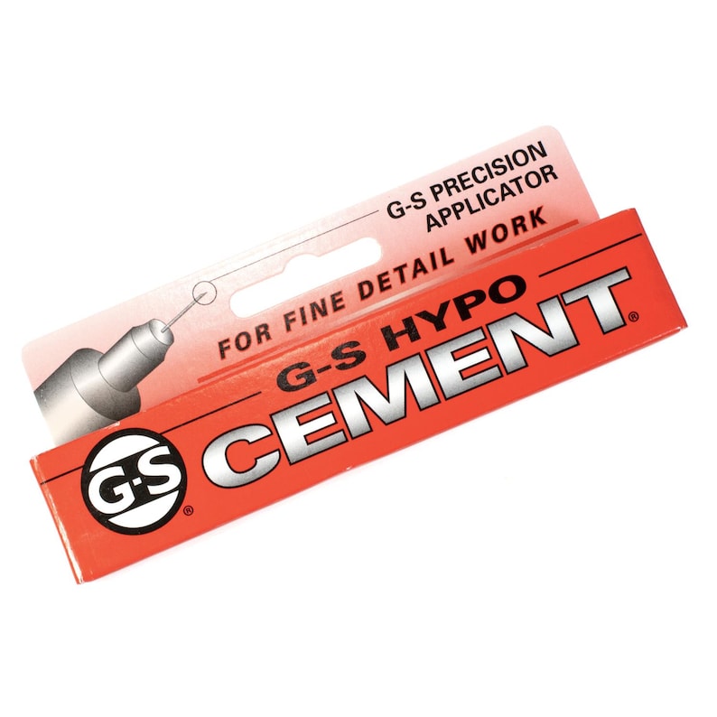 Puede incluir: Un tubo rojo y negro de G-S Hypo Cement con un aplicador de precisi&oacute;n para trabajos de detalle fino. El tubo tiene una etiqueta blanca con texto negro y un logotipo en blanco y negro.