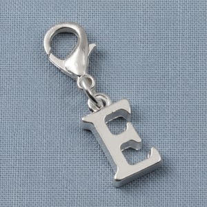 May include: A silver-toned metal charm in the shape of the capital letter E. The charm features a smooth, reflective surface and is attached to a functional lobster claw clasp, allowing it to be easily clipped onto various items or jewelry pieces.
