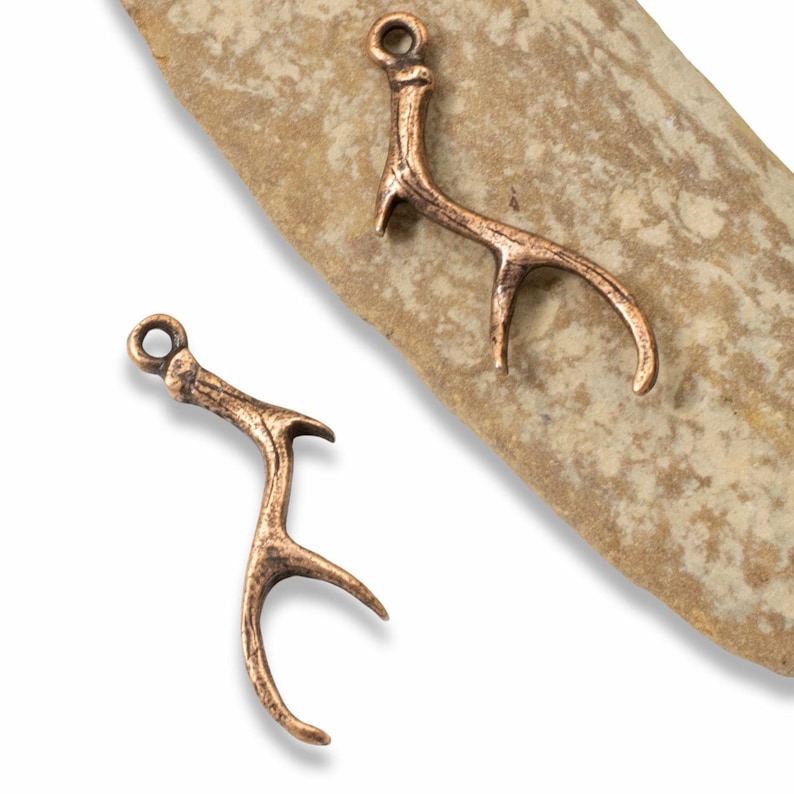 a pair of copper antler charms sitting on top of a rock