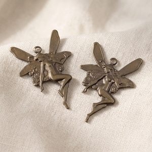 May include: Two antique bronze-toned metal charms, each shaped like a winged fairy figure in a seated pose. The charms feature detailed wings and a small circular loop at the top for attachment, showcasing a metallic finish with dark highlights.