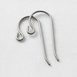 May include: Two silver-toned metal earring hooks with a smooth, curved design. Each hook features a rounded top loop for attachment and a long, slender wire that extends downward, forming a classic shepherd hook shape for jewelry making.
