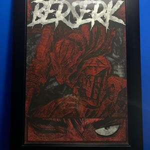 May include: A framed print of a black and white illustration of a character from the manga series Berserk. The character is wearing a helmet and armor. The title "Berserk" is written in silver lettering at the top of the print.